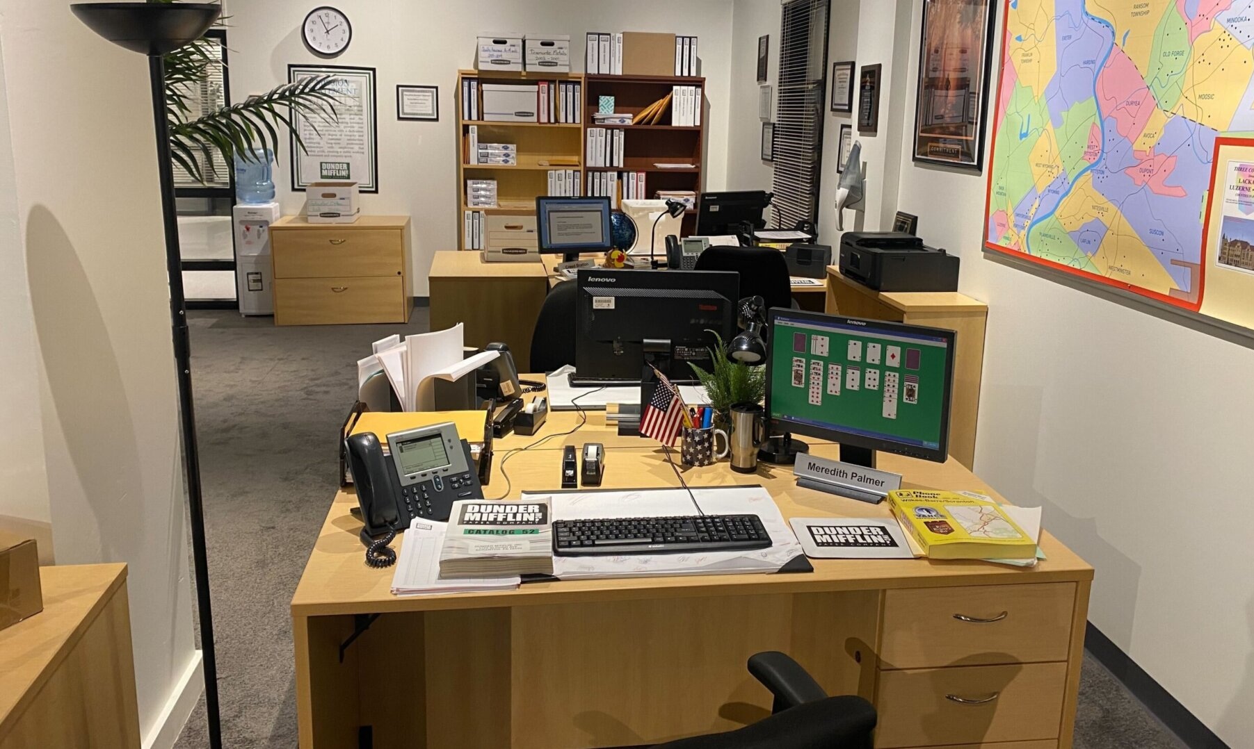 Desk area of Meredith Palmer with open space in the background at Dunder Mifflin.